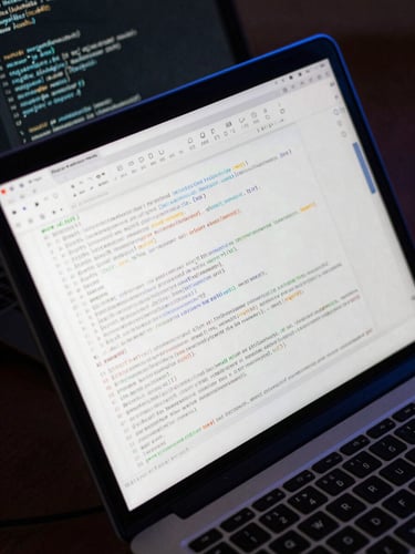 Close-up overhead view of a laptop screen showing a chat interface with dense JSON response data, terminal window reflected in the screen glass, cool blue monitor glow on a dark desk surface