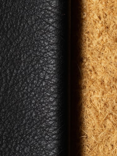 Macro studio shot of thick black full-grain leather grain next to raw textured golden wool, high contrast, deep shadows, 85mm lens