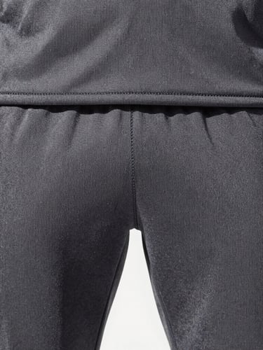 Close-up of reinforced flatlock stitching on a charcoal performance tracksuit, bright daylight, high-contrast crisp tones