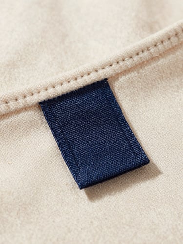 Macro shot of a heavy-weight organic cotton garment collar with a custom-woven fabric label stitched precisely, natural daylight, soft shadows
