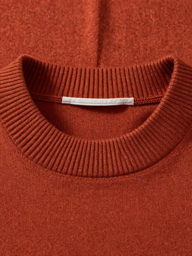 A high-definition macro shot of a heavy-weight burnt terracotta cotton sweater with a clean, custom-milled ribbed collar, soft natural side lighting.