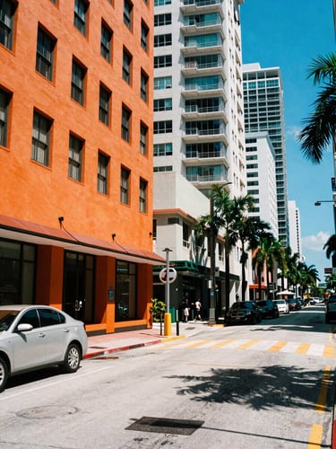 High-contrast urban Miami streetscape at high noon, sharp graphic shadows, vibrant orange and electric blue accents, 35mm editorial photography.