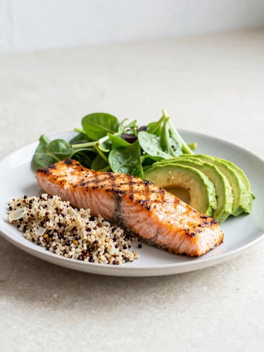 Approach shot of a colorful, fresh, portion-controlled balanced plate with grilled salmon, avocado, quinoa, and fresh greens on a light stone counter under soft daylight.