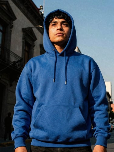 Gritty editorial streetwear photography, low-angle heroic shot of a supporter wearing a heavy cotton blue hoodie in CDMX urban streets, late-afternoon sun, 35mm film grain.