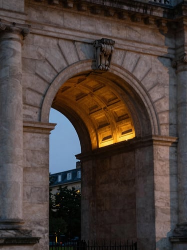 A close-up dramatic shot of a classical stone university archway illuminated by a warm golden light source, deep twilight shadows framing the architecture.