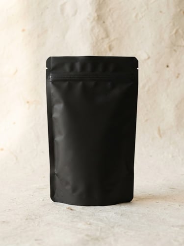 Minimalist studio photography of the Arpo Café Especial Black package, a clean matte black 250g coffee bag standing centered on a textured off-white background, soft diffused daylight, warm earth tones, editorial composition, 50mm lens.