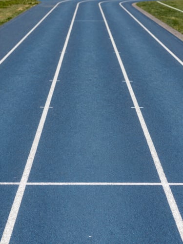 A clean, bright shot of a modern athletic facility track with crisp white lines, natural daylight, professional environment