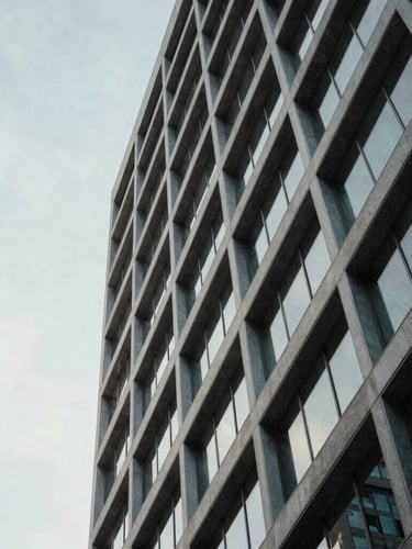 Abstract modern corporate building facade with sharp diagonal lines, steel and glass under soft natural light, minimalist composition, negative space on the left.