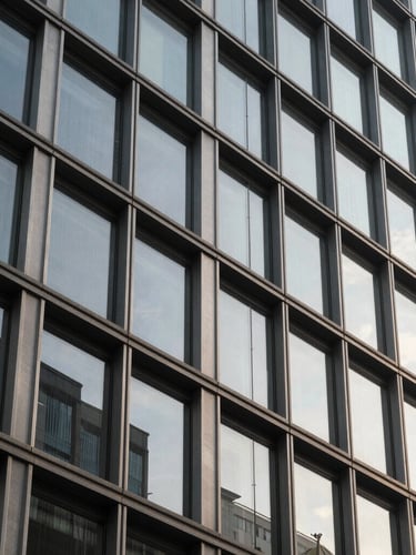 Detailed architectural close-up of a modern corporate building facade, sharp geometric lines of steel and glass, soft natural morning light with subtle shadows, professional and sober tone.
