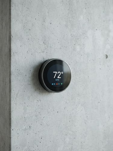 Sleek, modern smart thermostat integrated seamlessly into a minimalist concrete wall, bright indirect daylight, cool desaturated tones, sharp focus, high-end consumer electronics aesthetic.