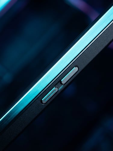 Extreme macro close-up of a premium mobile device edge, sharp metallic bezel reflecting glowing neon cyan light, dark moody background with deep blue shadows, high-contrast tech aesthetic.