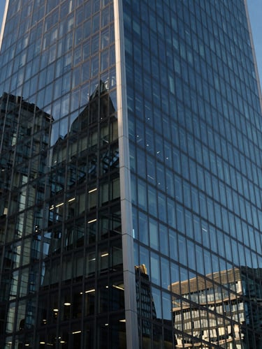 High-contrast architectural angle of a modern skyscraper in London, sharp shadows, cool blue hour light reflecting off glass facade.