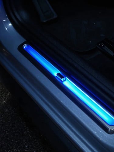 Close-up of a car door threshold with an LED door sill, highlighting the small magnetic trigger placement on the door frame, moody lighting, neon blue glow, 35mm lens