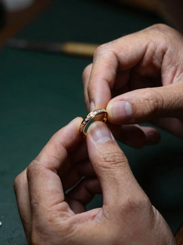 Close-up of a master jeweller's hands holding an elegant gold bridal ring under dramatic low-key directional lighting, 85mm lens