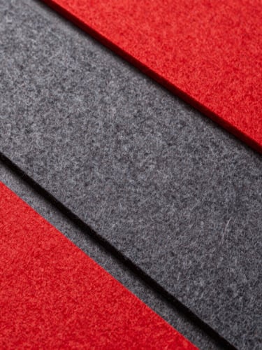 Overhead flat-lay of precision-cut synthetic felt bags and acoustic panels in vibrant red and deep gray, clean sharp studio lighting, minimal composition.