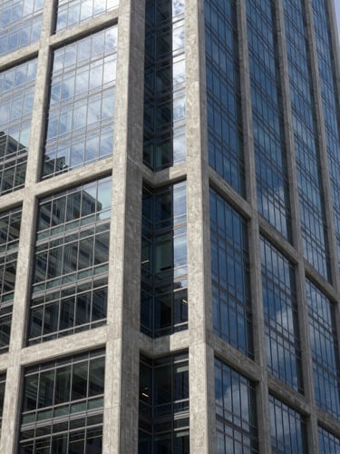 A sharp architectural detail of a modern financial skyscraper in Miami, concrete and reflective glass meeting at a sharp angle, cool crisp daylight, deep silver shadows.