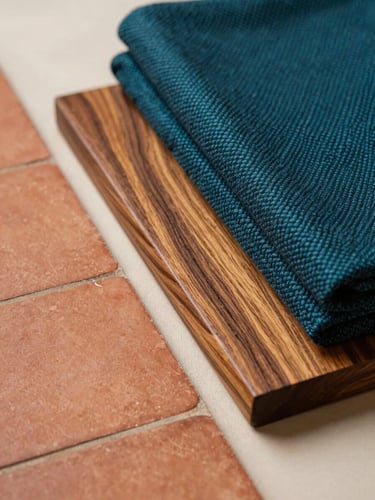 A close-up of tactile regional materials, featuring warm terracotta tiles, polished local teak wood, and deep teal handwoven textiles resting on a soft ivory surface.