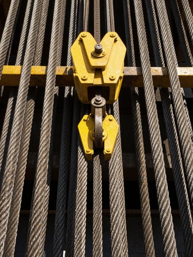 Close-up of industrial steel rigging gear and heavy cables glinting in the bright daylight, yellow steel accents, sharp focus
