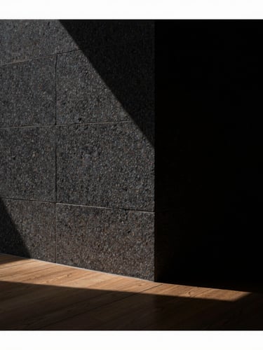 Straight-on architectural detail of a dark honed Belgian bluestone wall meeting a fumed oak floor, razor-sharp shadow line, dramatic low-key side lighting, medium format texture shot