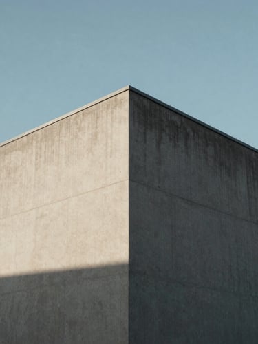 Minimalist urban building corner against a clear sky, strong diagonal shadow on concrete facade.