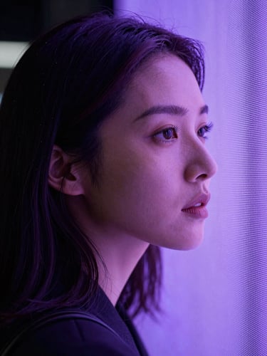 Cinematic portrait of a woman looking thoughtfully past a glowing screen, soft volumetric purple light, high-contrast editorial style.