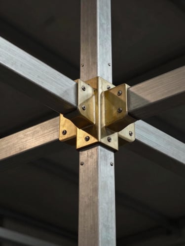 Macro architectural crop of brushed steel and champagne-gold structural joints of a custom-built event pavilion, low-key dramatic lighting.