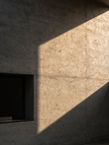 Tight portrait-aspect architectural crop of a raw board-formed concrete wall casting deep geometric shadows under warm golden hour light, 35mm lens.