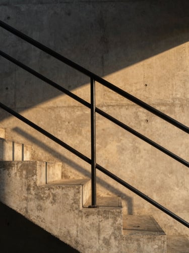 Cinematic architectural crop of a raw concrete staircase, warm golden-hour light casting long shadows across matte black metal railings, 35mm lens.