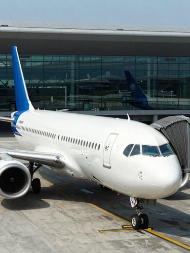A crisp eye-level shot of a premium commercial airplane parked at a sleek modern airport terminal gate, high-contrast daylight, reflections on the glass terminal, professional travel aesthetic.