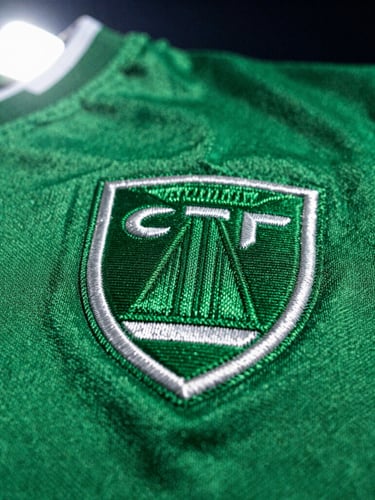 Close-up macro shot of a football shirt embroidery badge, pristine stitching details, vibrant green fabric, dramatic stadium lighting