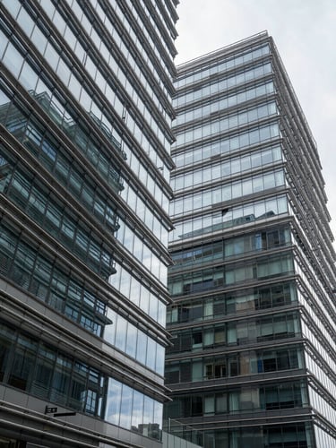Wide panoramic shot of modern corporate architecture with sharp steel and glass diagonal structures, cool daylight reflecting off metallic surfaces, high contrast.