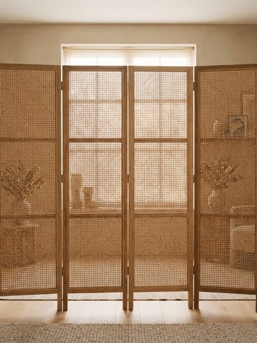 Straight-on architectural medium format photograph of a folding rattan screen filtering soft morning light in a warm minimalist apartment, sand and natural oak tones.