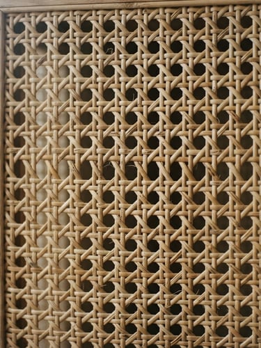 Close-up of natural woven rattan screen texture, soft diffused side-lighting from a window, muted sand tones, architectural detail