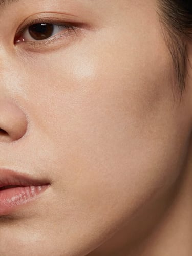 Close-up of cheek skin showing slight texture and uneven tone under soft directional studio lighting, 35mm clinical aesthetic