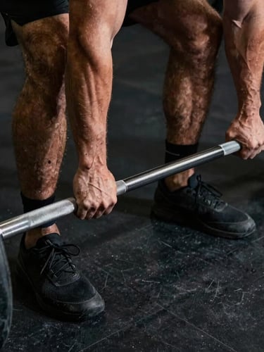 Tight, high-contrast shot of Nick's hands gripping a heavy steel barbell in a dark, industrial San Diego gym, dramatic overhead lighting casting deep shadows, raw concrete background.