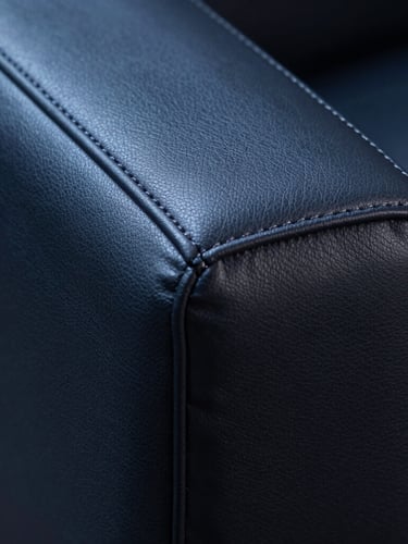 Macro close-up of premium dark leather upholstery with precise stitching, clinical studio lighting with cool blue tones, side angle