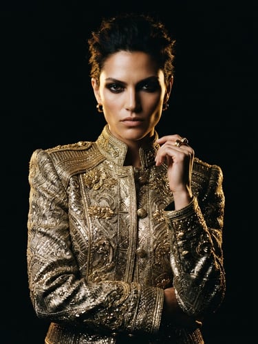 Moody editorial fashion photography, model wearing structured gold-threaded jacket, dark studio backdrop, dramatic low-key lighting, golden rim light