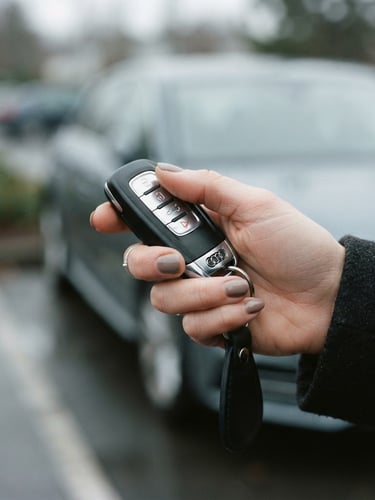 A close-up of a hand holding modern car keys outside, soft natural overcast daylight, muted cool tones, 35mm lens, shallow depth of field