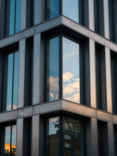 Dramatic close-up of a modern brushed steel and glass corporate facade in Budapest, sharp focus, cool blue tones with warm golden-hour window highlights, 35mm lens.