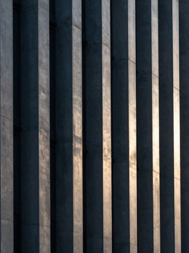 Abstract geometric pattern of light and shadow on a modern concrete facade, clean vertical lines, cool charcoal and silver tones, sharp focus