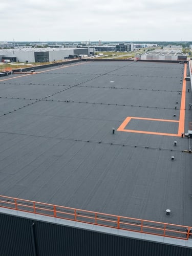 Wide-angle industrial drone shot of a perfectly finished clean flat roof with dark grey bitumen membrane, overcast daylight, sharp contrast, charcoal and safety orange tones, 35mm lens, high detail