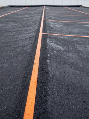 Close-up of a perfectly sealed roof seam on a commercial building, charcoal bitumen texture, safety orange marking lines, sharp focus