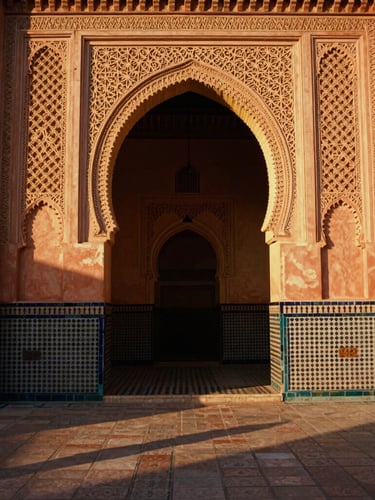 Wide-angle architectural shot of an intricate Islamic archway in Morocco, golden hour sunlight casting long shadows on terracotta mosaic tiles, 35mm film.