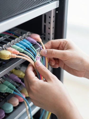 Hands-on tech support, close-up of friendly hands neatly organizing colorful pastel ethernet cables into a clean office server rack, bright natural lighting, 35mm.