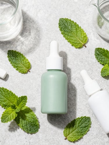 Top-down product flat-lay of organic dental ingredients, green mint leaves, clean laboratory glassware on a light grey stone surface, bright natural daylight