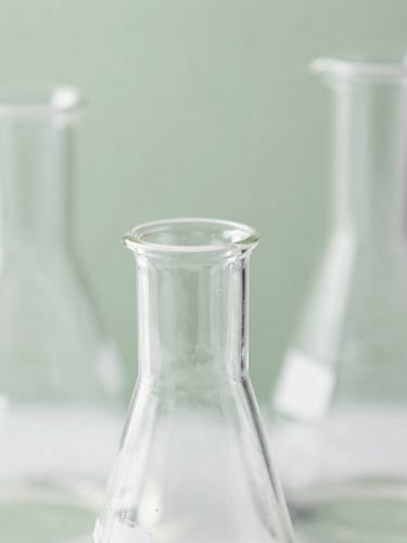 Macro photograph of clean scientific laboratory glassware reflecting bright diffused daylight, soft sage green background, high detail editorial photography