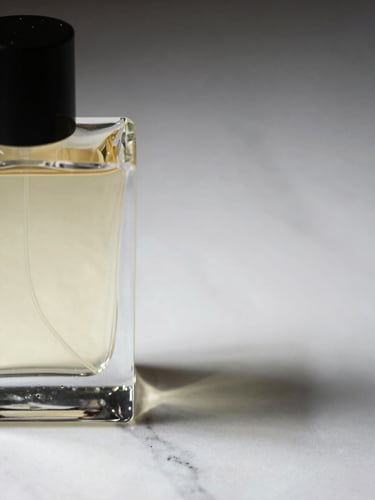 Close-up detail of a luxury perfume bottle resting on a white marble surface, shot from slightly above at a three-quarter angle, studio strobe lighting from the left casting a clean shadow to the right, negative space filling the upper right third of the frame, no hands or background clutter