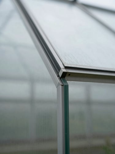 Macro close-up of a greenhouse glass panel edge, natural overcast daylight refracting across the surface, precise cut edge in sharp focus, minimal background, clean technical framing