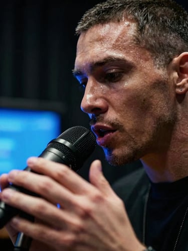 Extreme close-up of a rapper mid-delivery in a dark recording studio, electric-blue monitor glow raking across their face from the side, microphone in sharp foreground, expression intense and focused, motion blur on hands suggesting rhythm