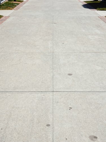 Straight-on architectural shot of a pristine concrete driveway and brick walkway, clean and free of stains, bright Wisconsin sun.